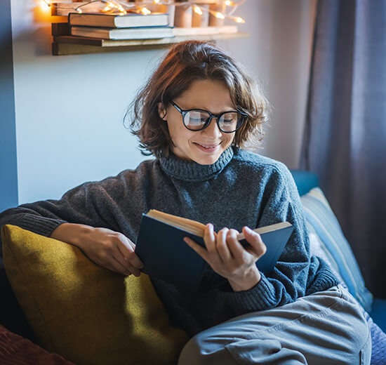 Frau mit einer Lesebrille liest ein Buch.
